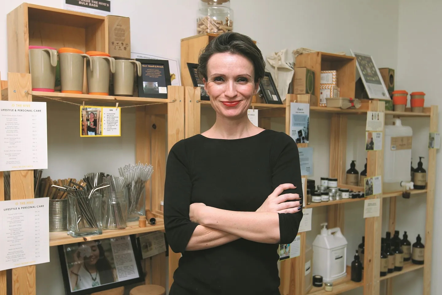 Claire standing arms crossed in The Hive's lifestyle and personal care aisle, shelves of unpackaged goods around her